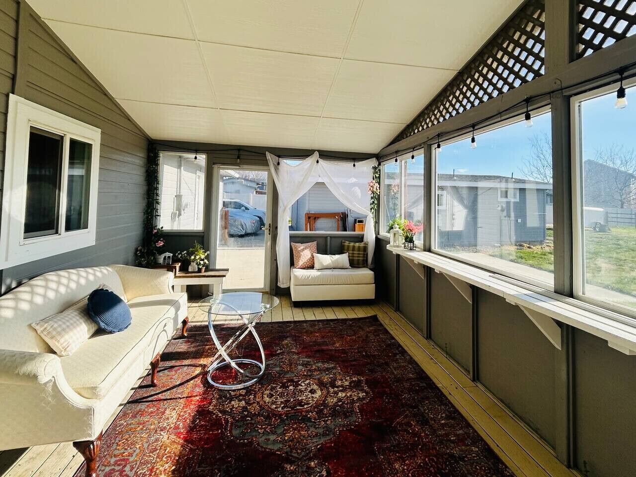 A sunroom with a sofa, a small table, a bed, and large windows.