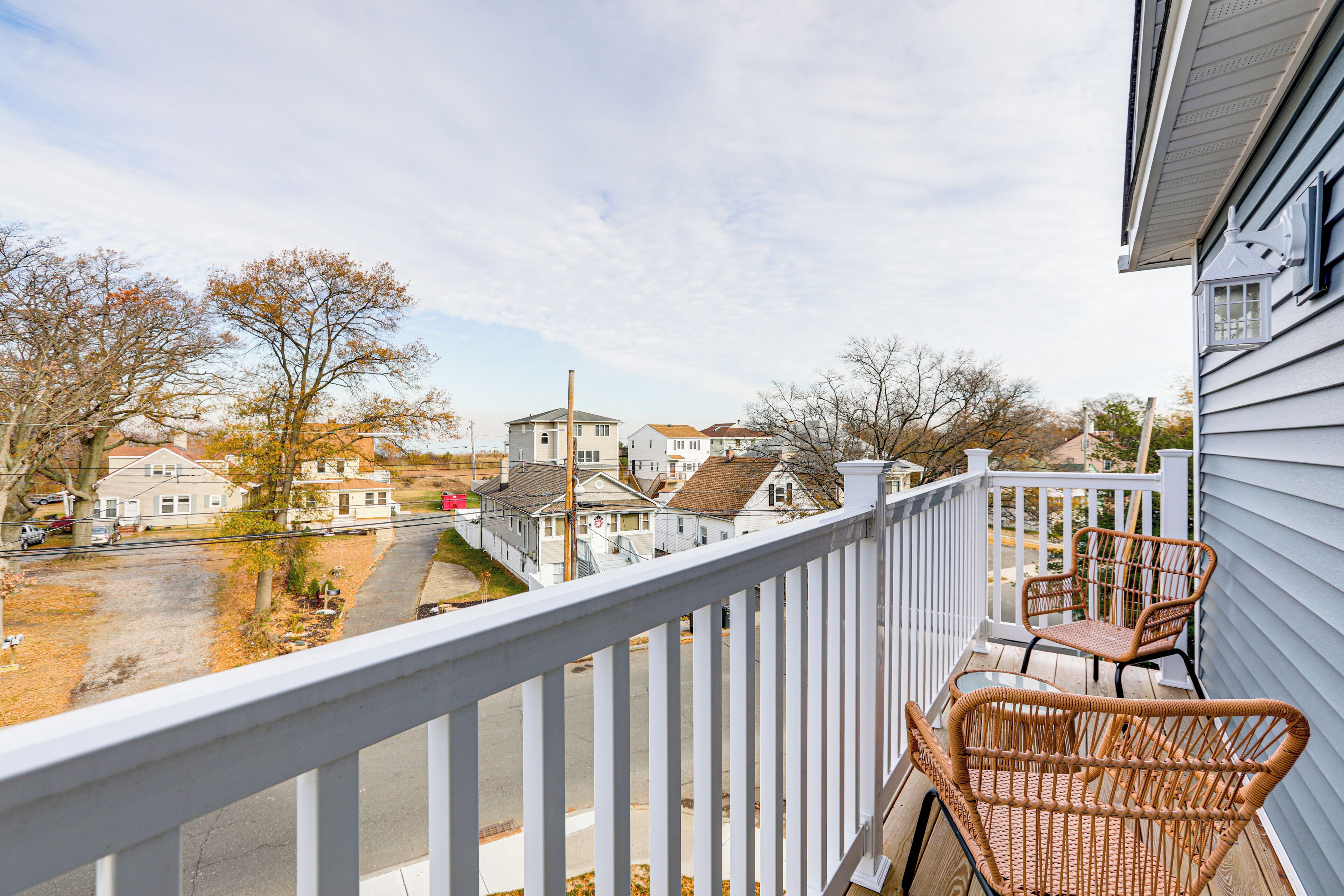 A balcony with wicker chairs and a view of a residential street.