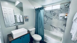Ein Badezimmer mit einem weißen Waschbecken, einer Toilette, einer Dusche mit Marmorwand und einem blauen Duschvorhang.