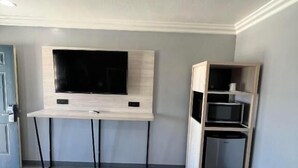 Ein Schlafzimmer mit Bett, Schreibtisch, Flachbildfernseher und integriertem Minikühlschrank.