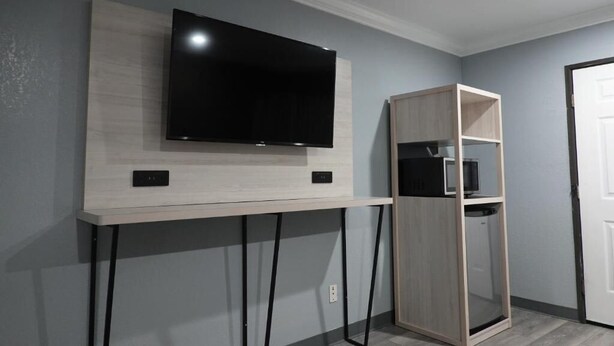 Ein Zimmer mit einem an der Wand montierten Flachbildfernseher, einer hellen Wandkonsole, einem Holztv-Schrank mit einer Mikrowelle und einer Tür rechts.