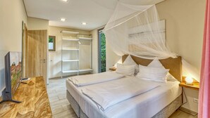 Quarto com cama sob dossel, mesa de cabeceira com abajur e piso de madeira.
