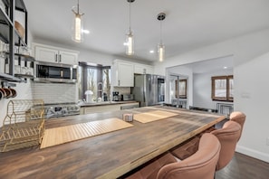 A modern kitchen with a wooden island, stainless steel appliances, pendant lighting, and a view to the outside.