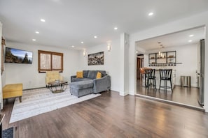 A spacious living area with a grey sectional sofa, a yellow armchair, and a dining area with a black table and chairs.