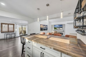 A modern kitchen with a central island, pendant lighting, and a dining area with a fireplace.