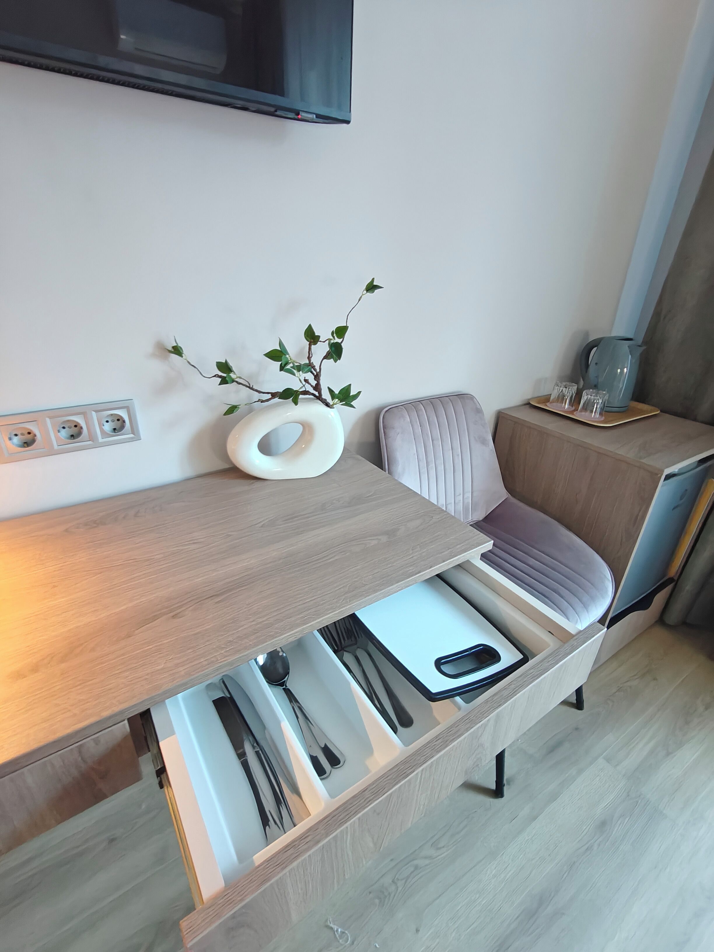 Une cuisine moderne dotée d’un plan de travail en bois intégré, d’une chaise rembourrée de couleur grise et d’une table d’appoint avec une bouilloire et des verres.