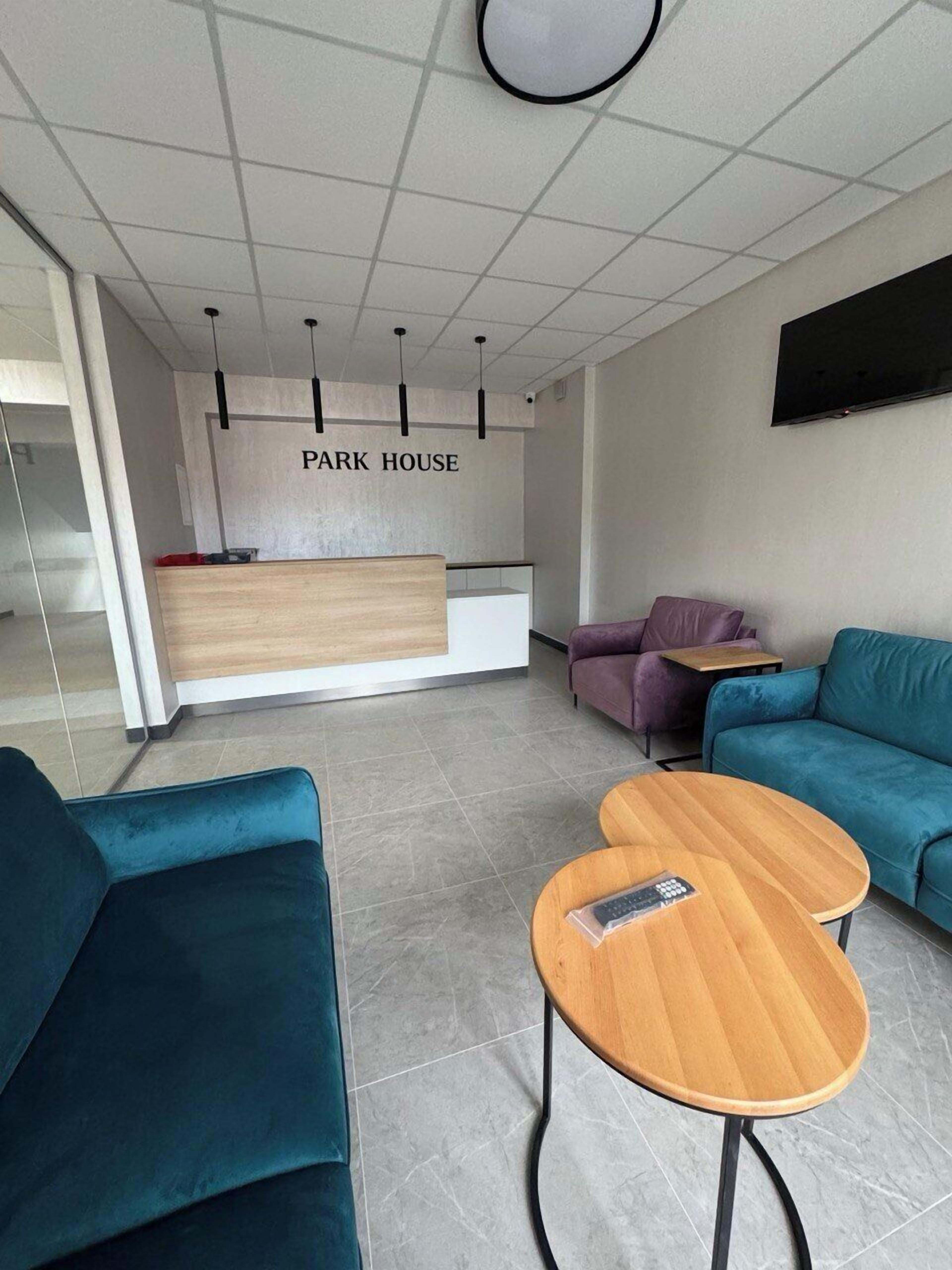 A modern reception area with a 'PARK HOUSE' sign, a wooden reception desk, teal sofas, and a round wooden table.