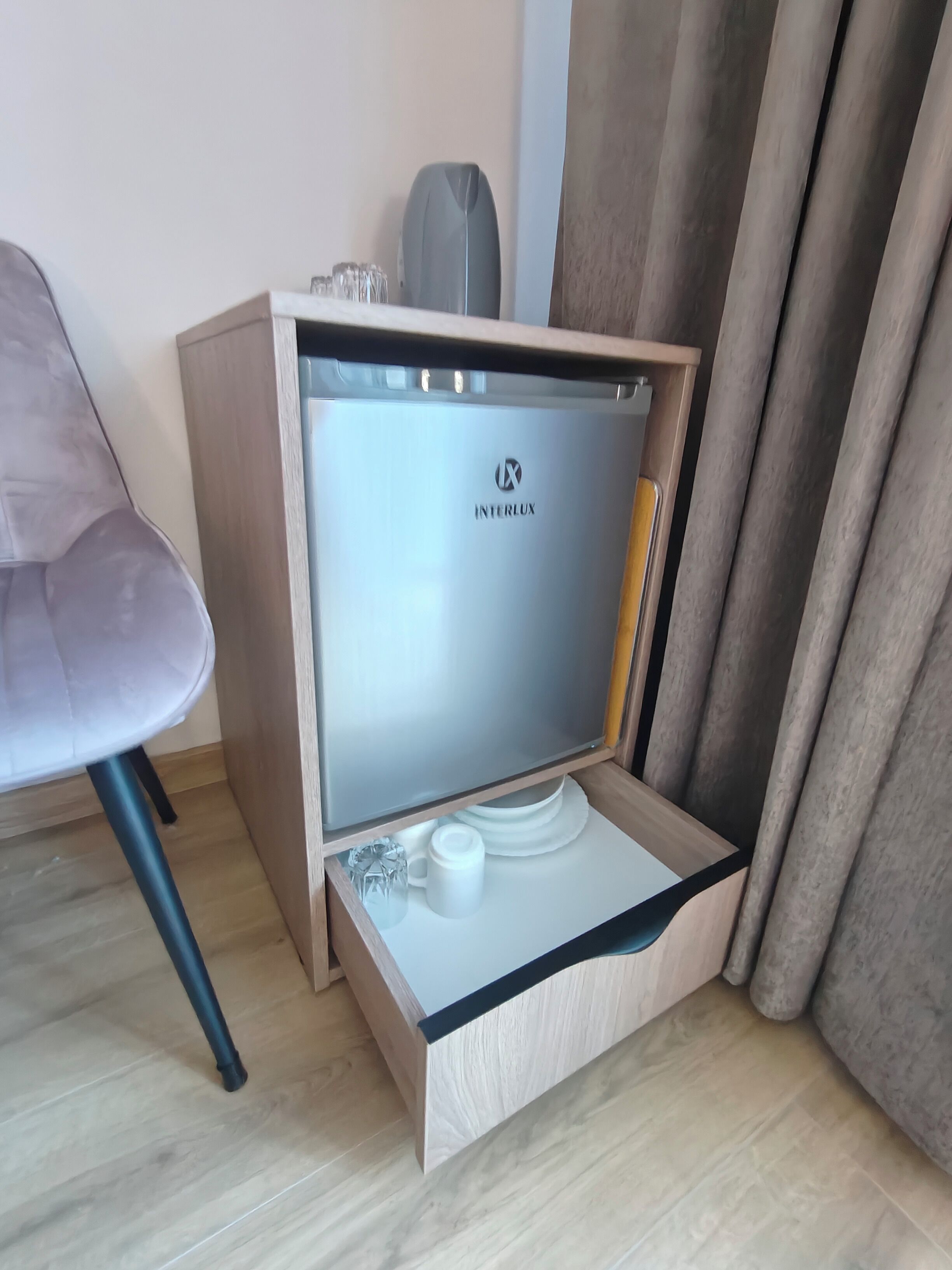 A compact minibar with a glass door, a small coffee maker, and a few glasses.