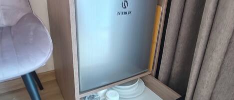 A compact minibar with a glass door, a small coffee maker, and a few glasses.