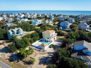 An aerial view of a coastal residential area with houses, a swimming pool, and a clear view of the ocean. - Corolla Getaway with Private Pool, 5 mins to Beach (Corolla)