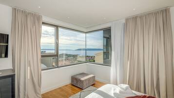 Una habitación de hotel moderna con un amplio ventanal que ofrece una vista panorámica del mar y el paisaje urbano.