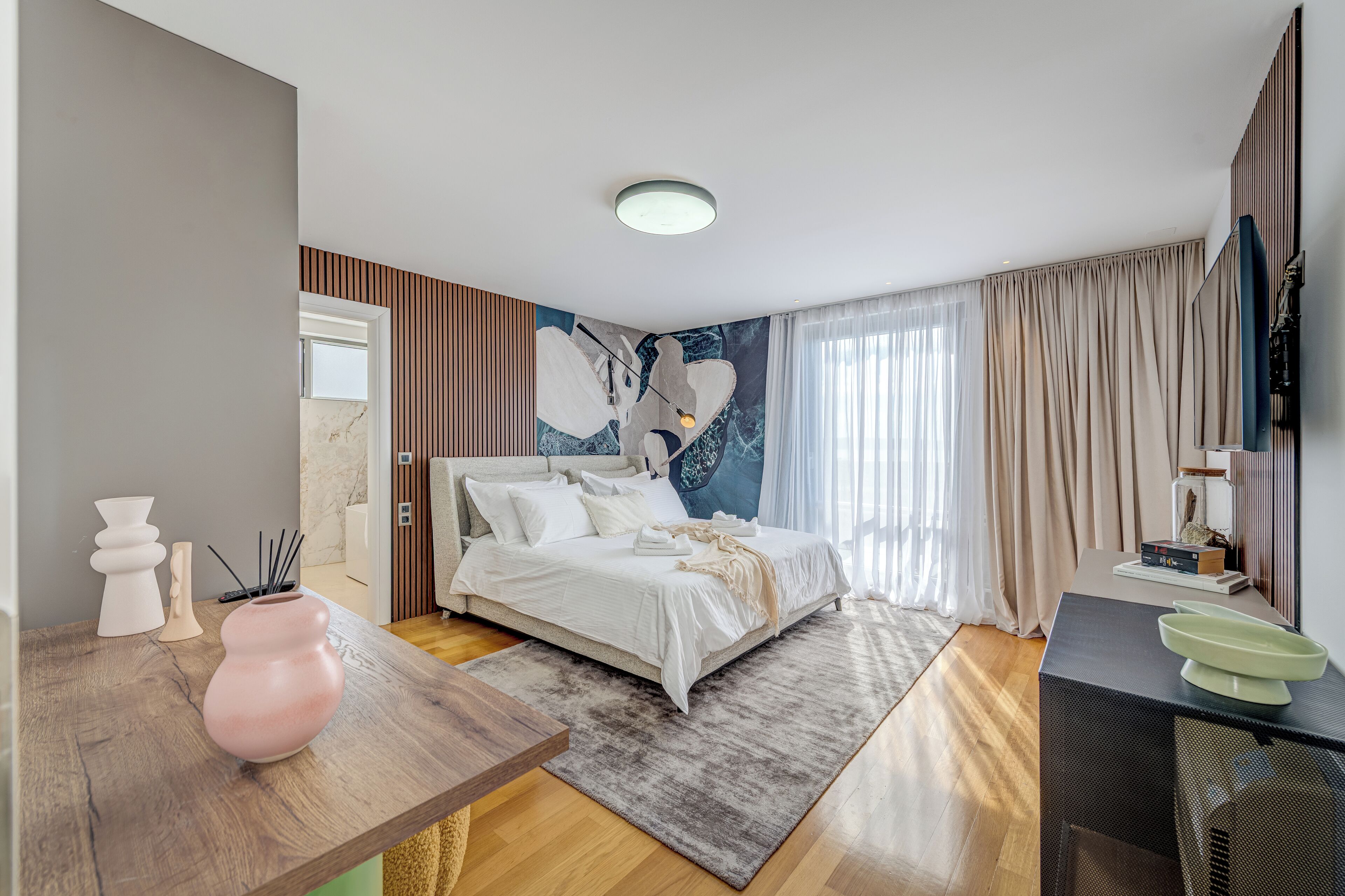 Una camera da letto moderna con un letto grande, una scrivania in legno, una TV e un murale sulla parete.