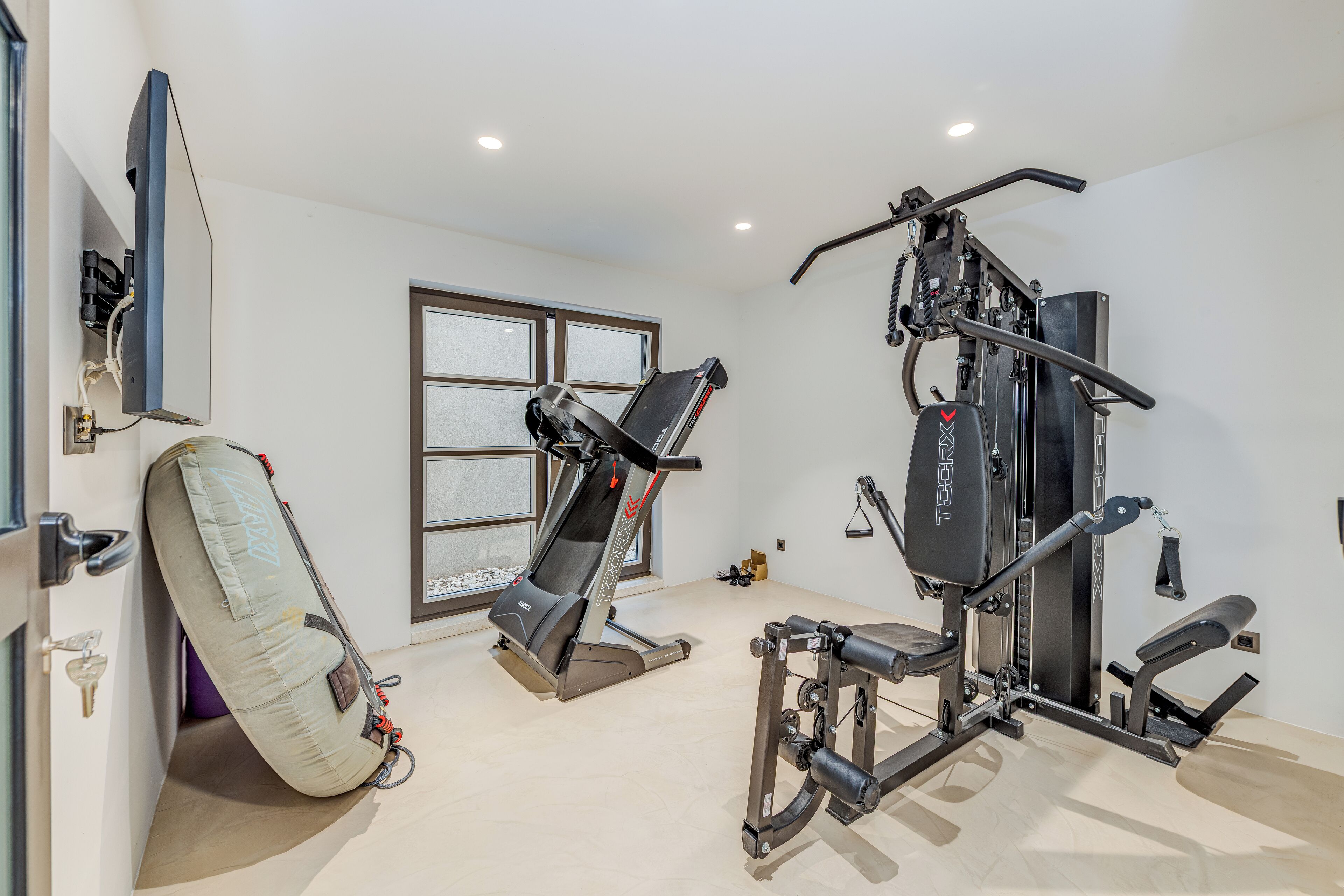 Une salle de sport équipée d’un tapis de course, d’une machine de musculation et d’un grand miroir.