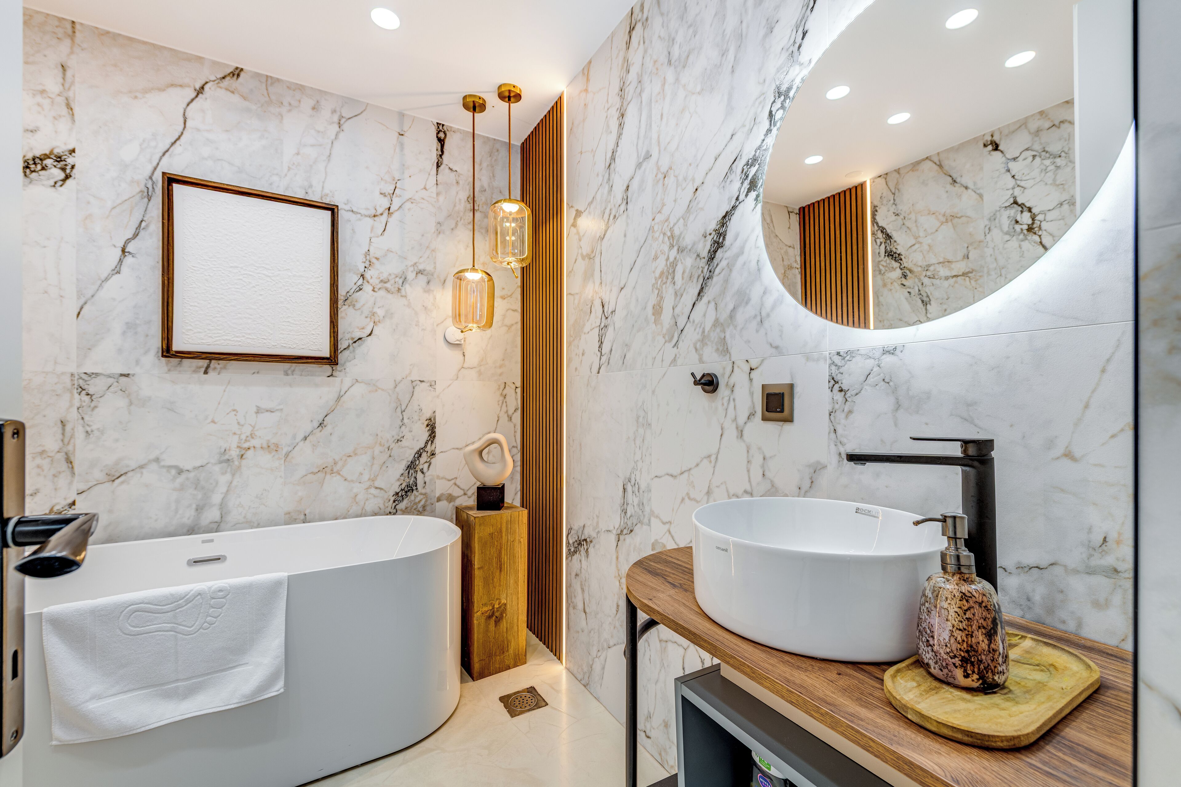 A modern bathroom with a freestanding bathtub, a large vanity with a round sink, and a mirror with a wooden frame.