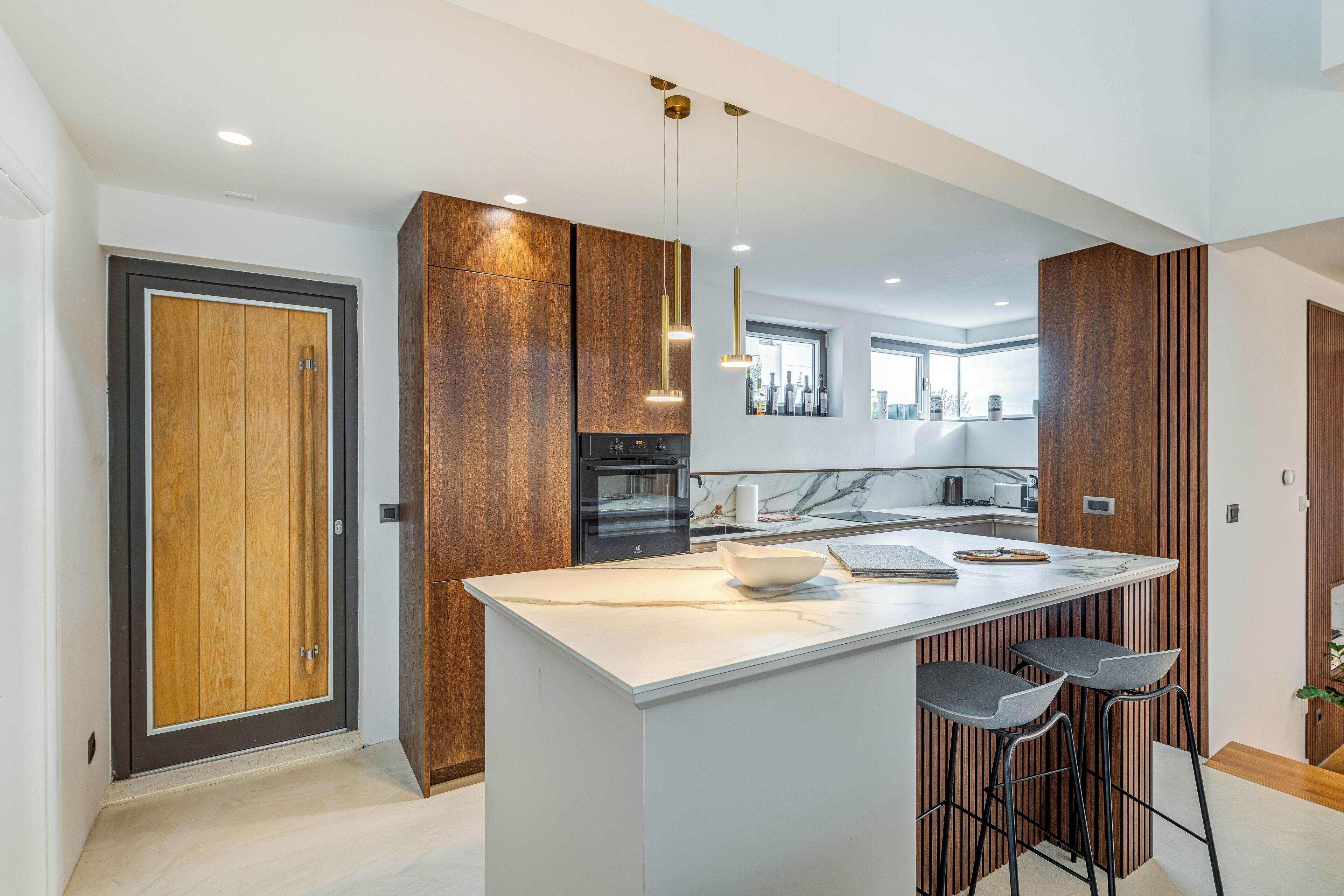 Une cuisine moderne dotée d’un îlot central, de tabourets de bar, de meubles en bois et de luminaires suspendus.