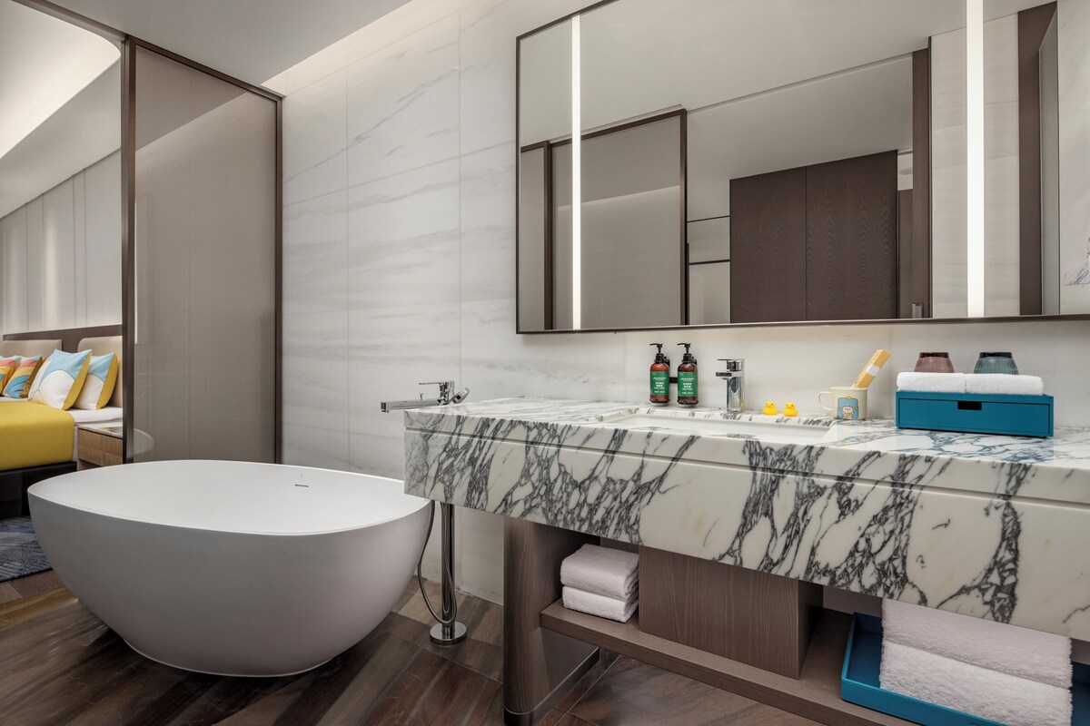A modern bathroom with a freestanding bathtub, a large mirror, and a marble countertop.