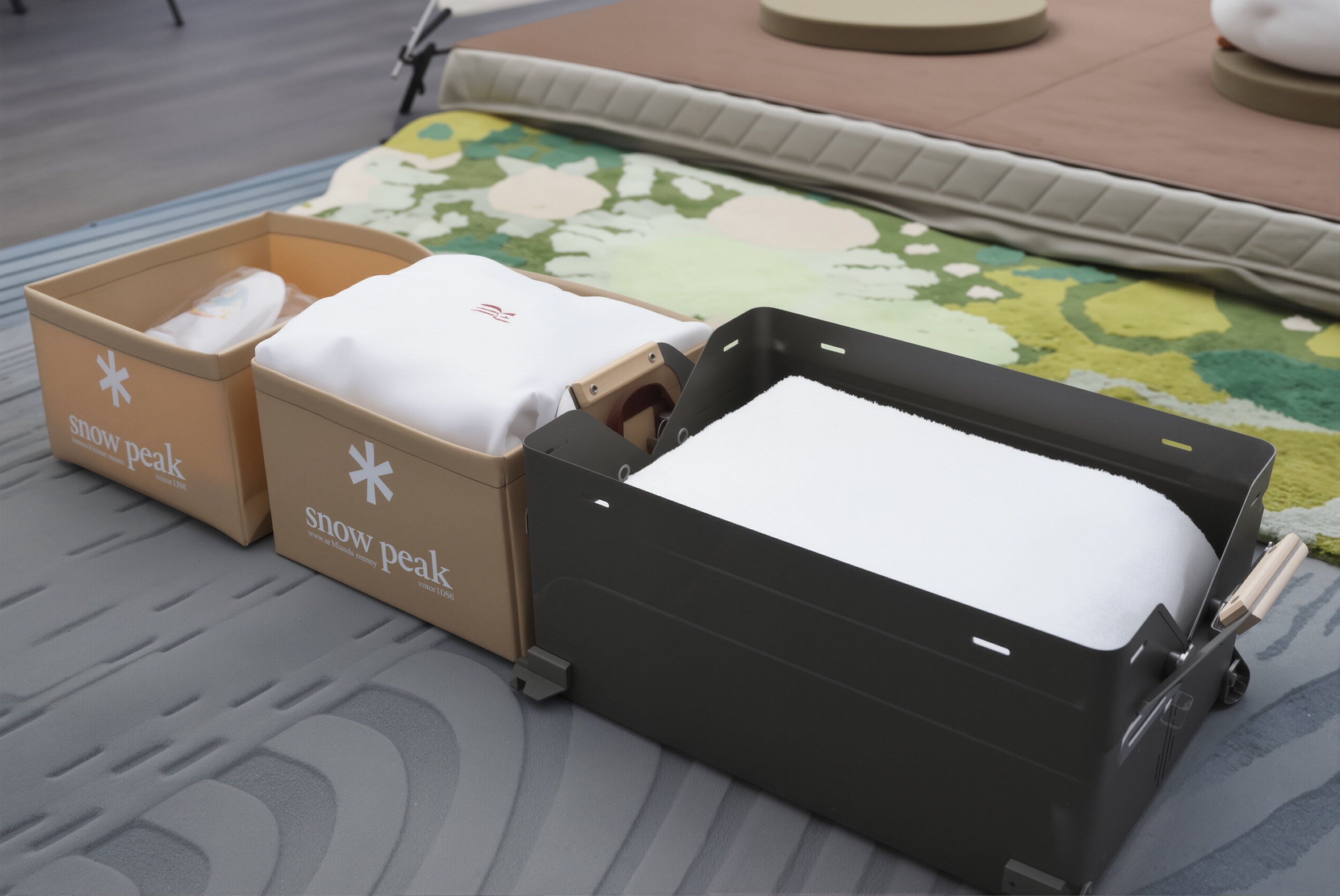 Three cardboard boxes with the text 'snow peak' and a black suitcase with a white towel.