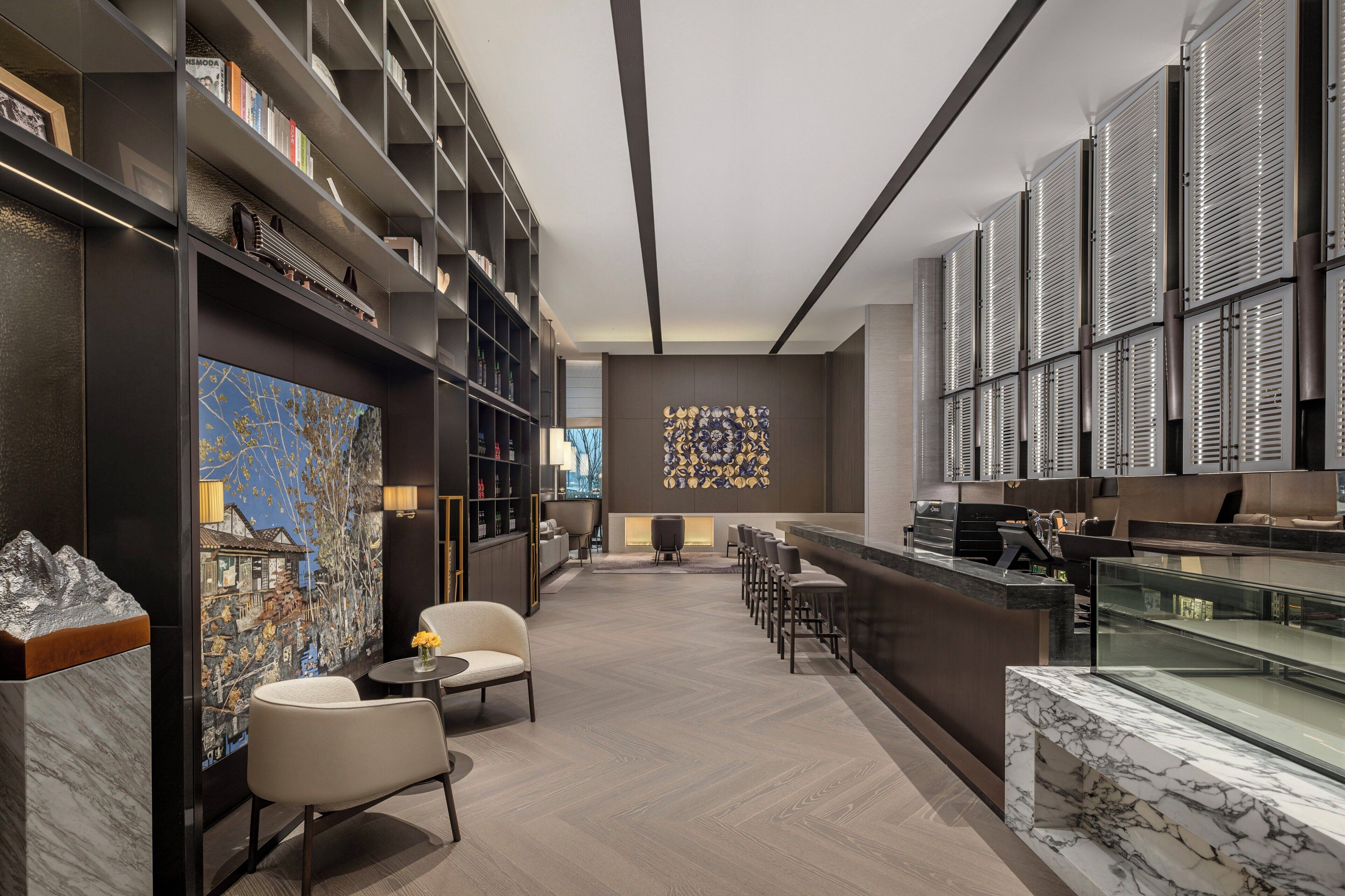 Un hall d’hôtel moderne doté d’un bar, de coins salon et d’une grande œuvre d’art abstraite qui orne un mur.