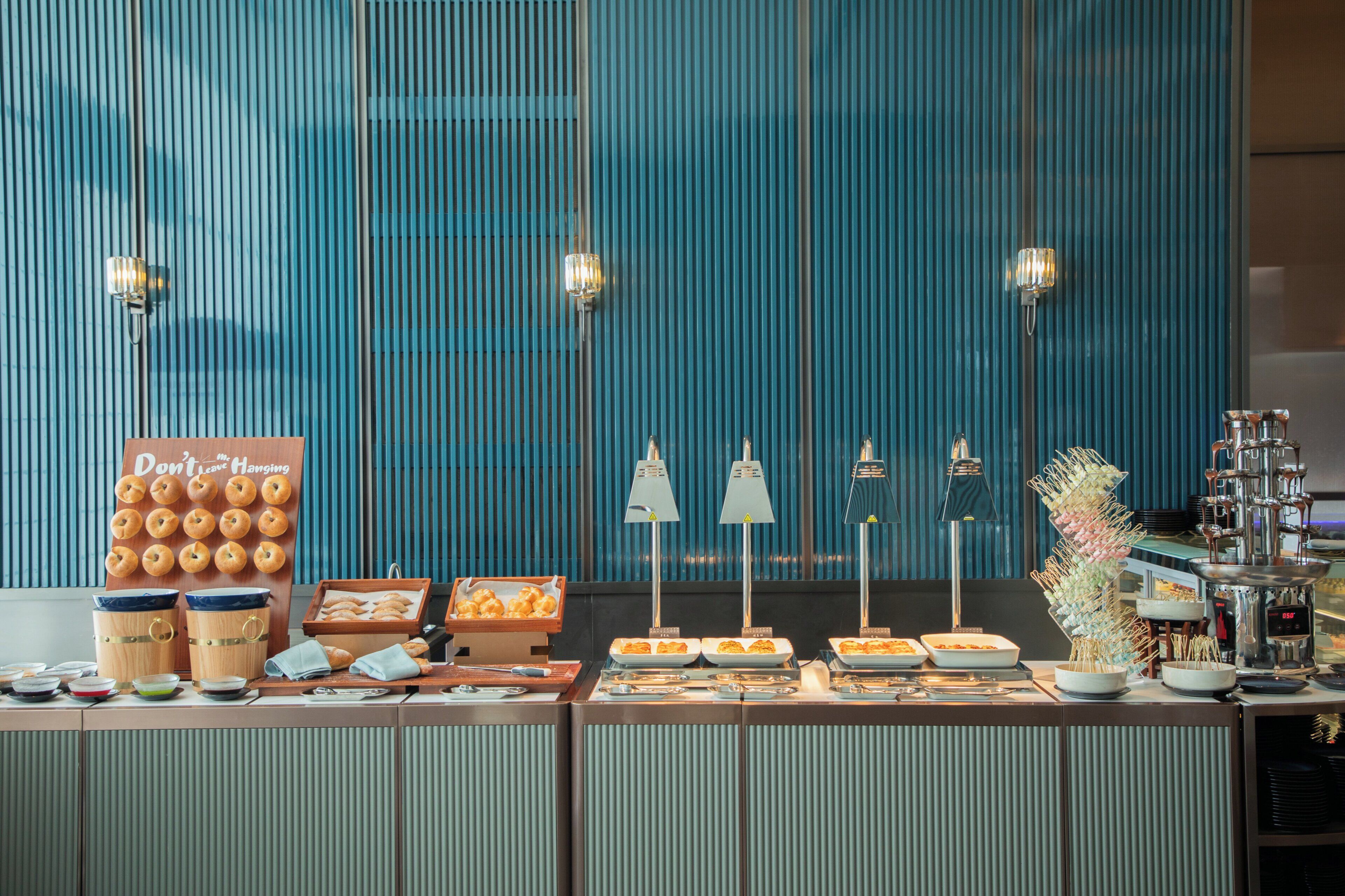 A buffet setup with various food items, a sign with a message, and a decorative plant.
