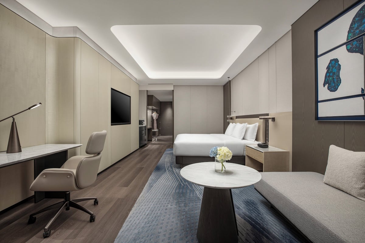 A modern hotel room with a bed, a sofa, a desk, and a TV.