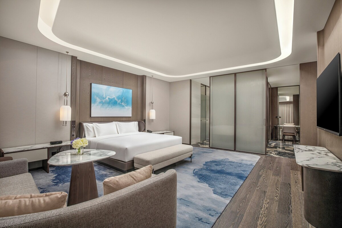 A modern hotel room with a large bed, a seating area with a coffee table, and a TV mounted on the wall.