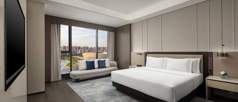 A modern hotel room with a large bed, a sofa, a TV, and a city view.