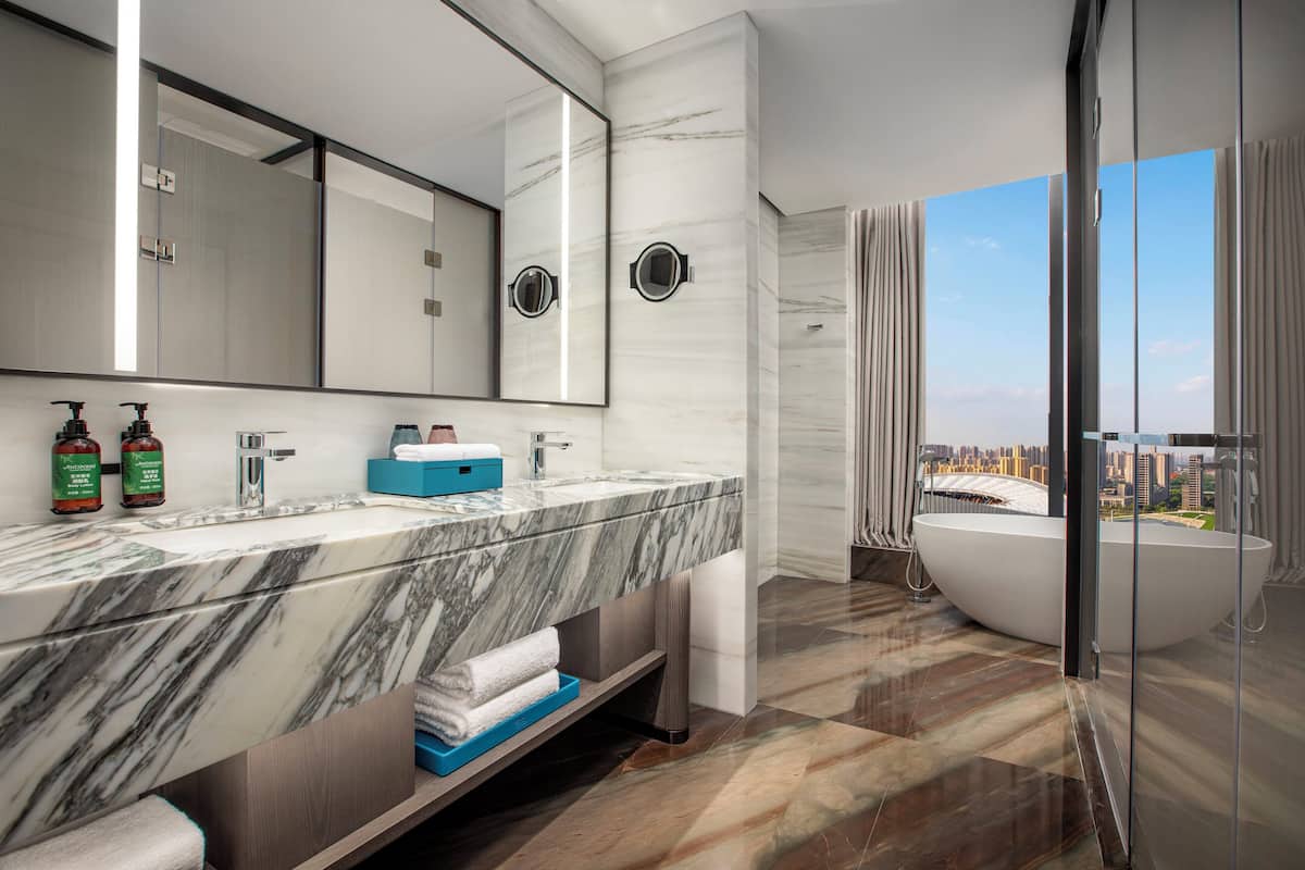 A modern bathroom with a marble vanity, a large mirror, and a bathtub.