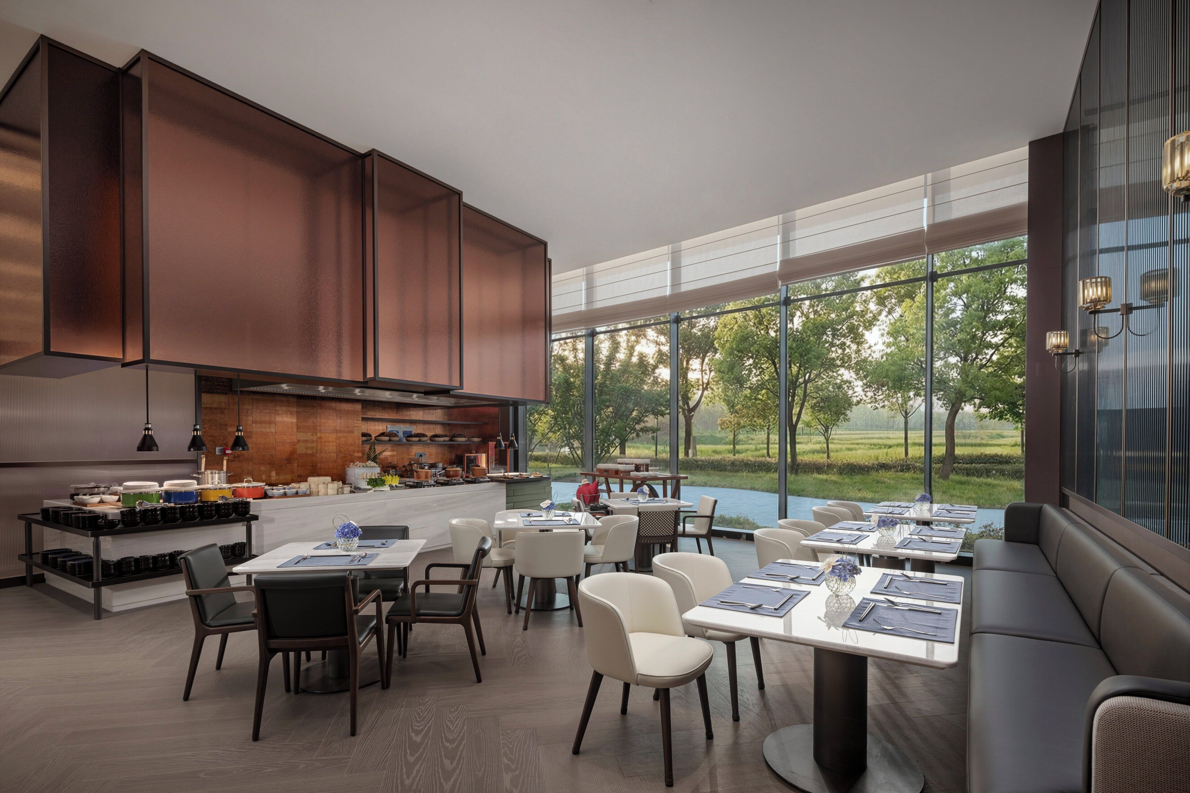A modern dining area with large windows, a kitchen with copper cabinets, and a view of the outdoors.