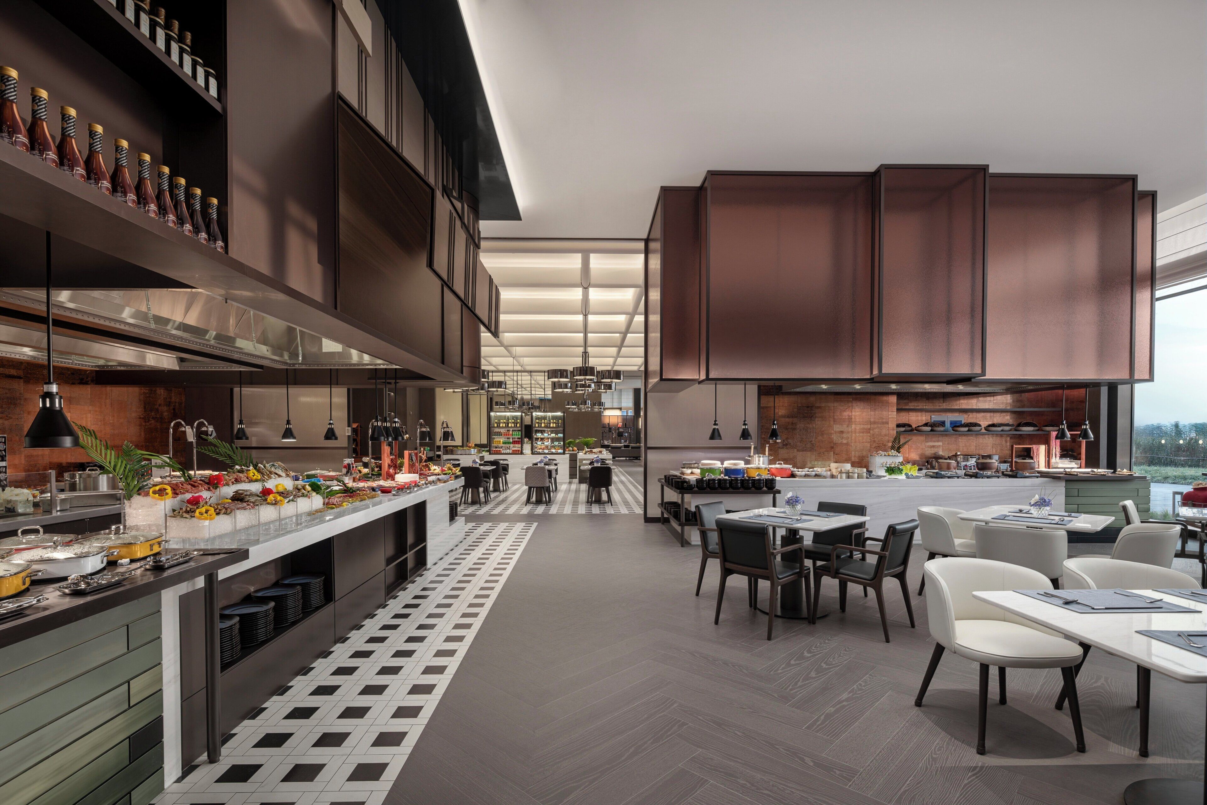 A modern kitchen with a central island, built-in appliances, and a dining area with tables and chairs.