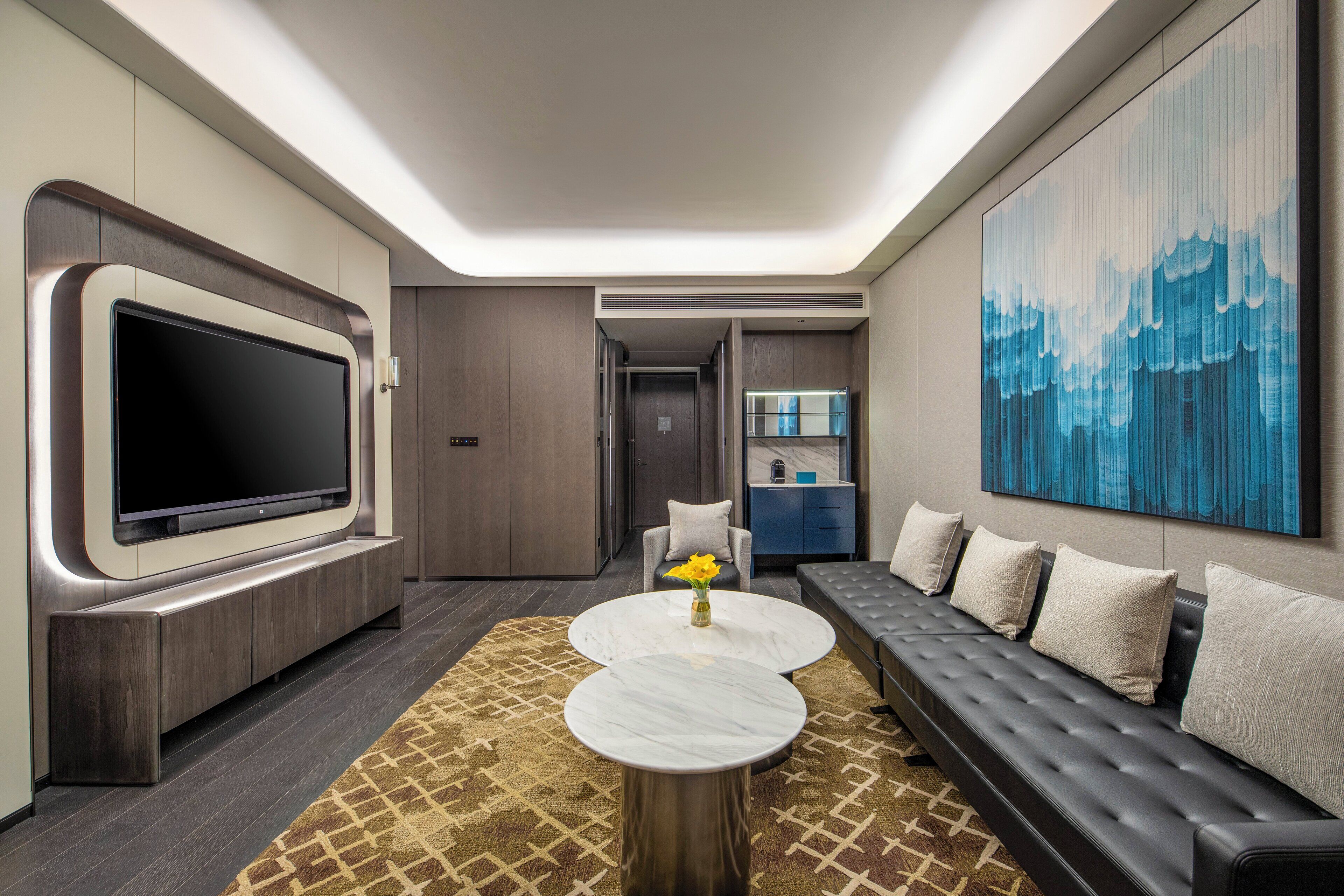 A modern living room with a large flat-screen TV, a sofa, a coffee table, and a patterned rug.