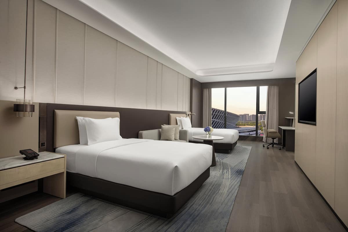 A modern hotel room with a large bed, a sofa, a desk, and a TV. The room has a city view.