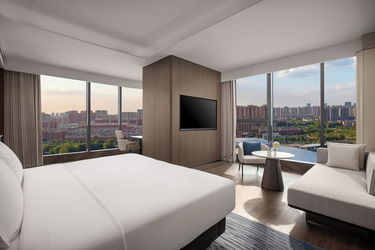 A modern hotel room with a large bed, a flat-screen TV, a sofa, and a dining table.