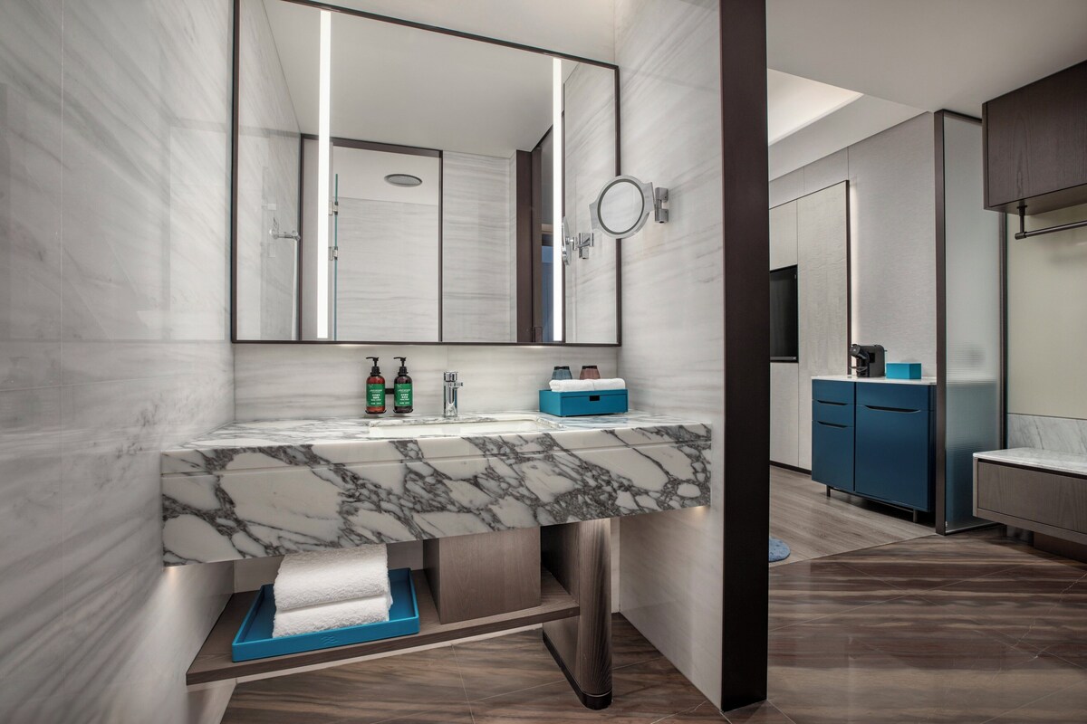 A modern bathroom with a marble sink, a large mirror, and a blue cabinet.