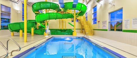 Une piscine intérieure avec un toboggan et des panneaux d’avertissement pour assurer la sécurité.