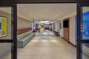 Un moderno vestíbulo de hotel con una zona de estar central, una recepción y un cartel de DEA.