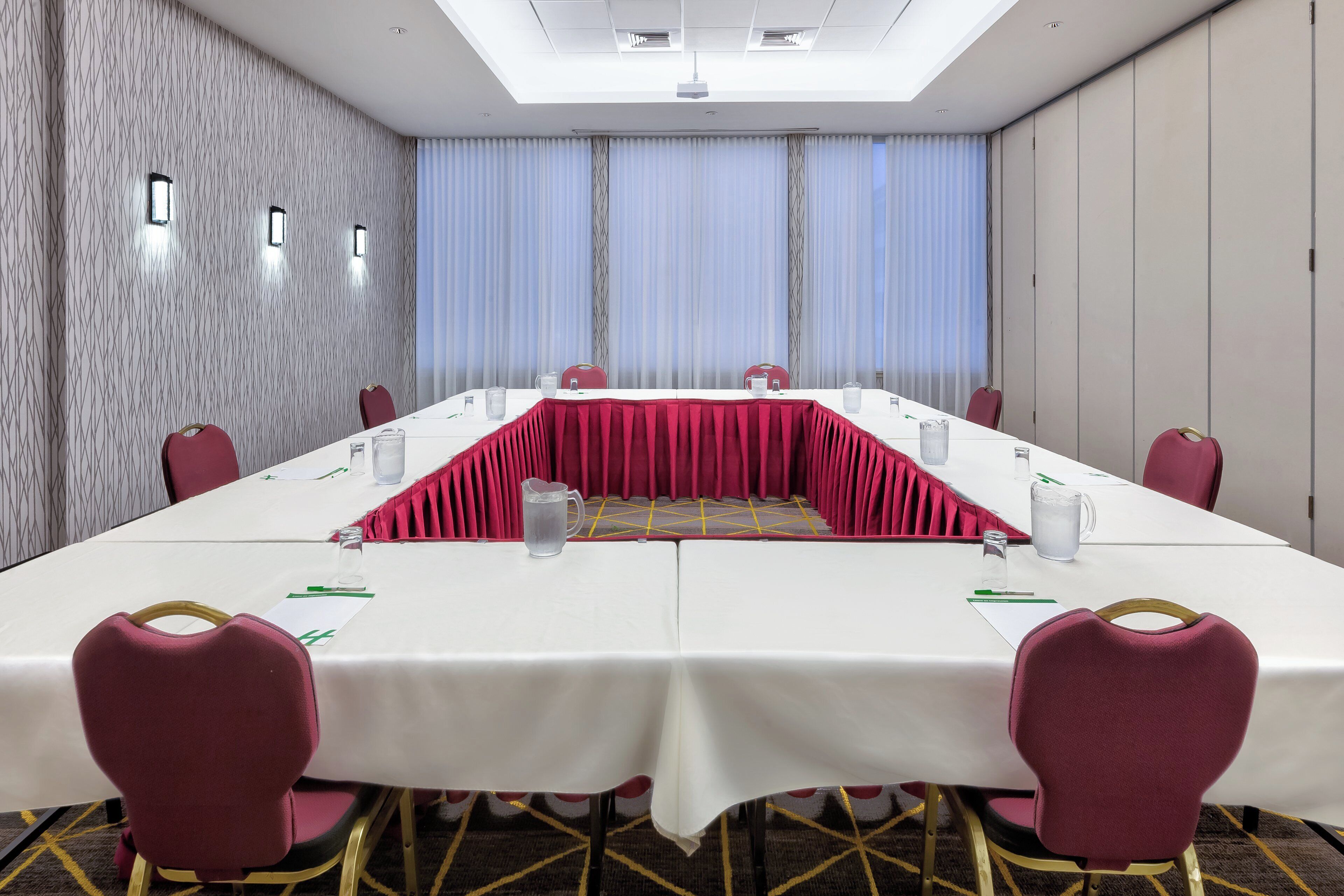 Une salle de conférence avec une longue table, des chaises rouges et un tapis à motifs.
