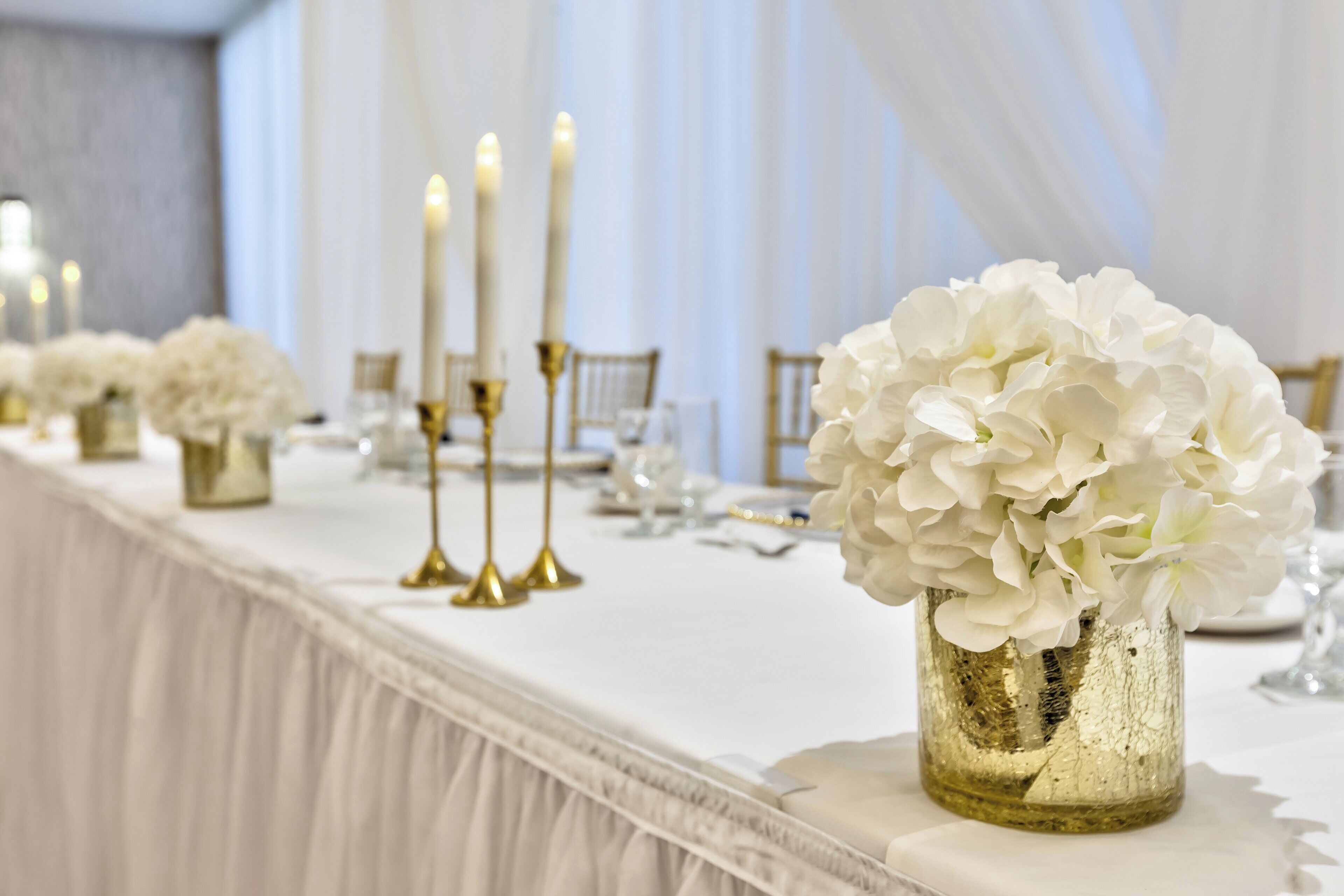 Una mesa de banquete con flores blancas, candelabros dorados y manteles blancos.