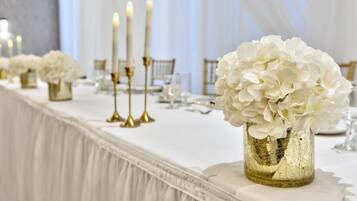 Una mesa de banquete con flores blancas, candelabros dorados y manteles blancos.