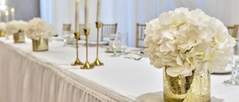 Una mesa de banquete con flores blancas, candelabros dorados y manteles blancos.
