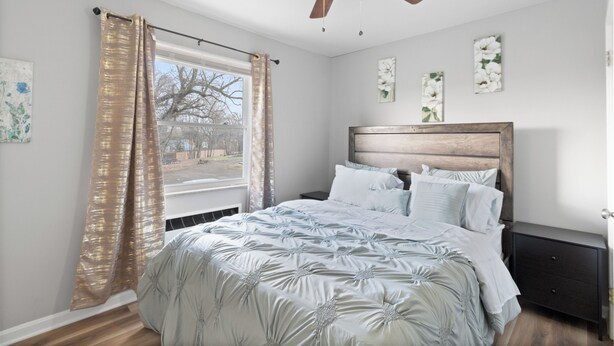 Un dormitorio con cama, mesita de noche, ventilador de techo y ventana con cortinas.