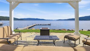 A covered patio with a view of a lake, a fire pit, and outdoor furniture. - Lakefront luxury with dock and views near Gozzer (Harrison)