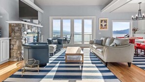 A spacious living area with a stone fireplace, a large window with a view, and a modern kitchen. - Lakefront luxury with dock and views near Gozzer (Harrison)