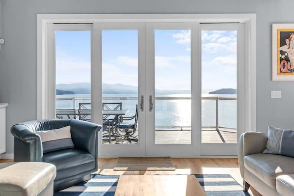 A living room with a view of a lake and mountains through large glass doors.