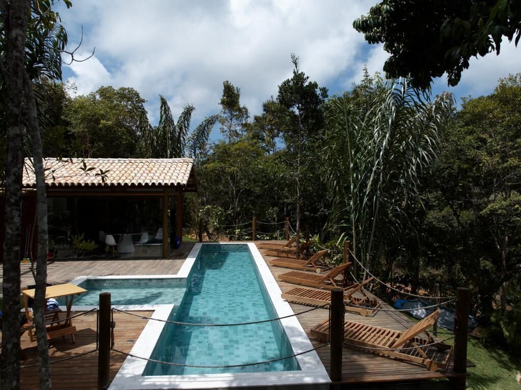 Une piscine rectangulaire dotée d’une terrasse en bois, entourée de chaises longues et d’un petit bâtiment dont le toit est recouvert de tuiles.