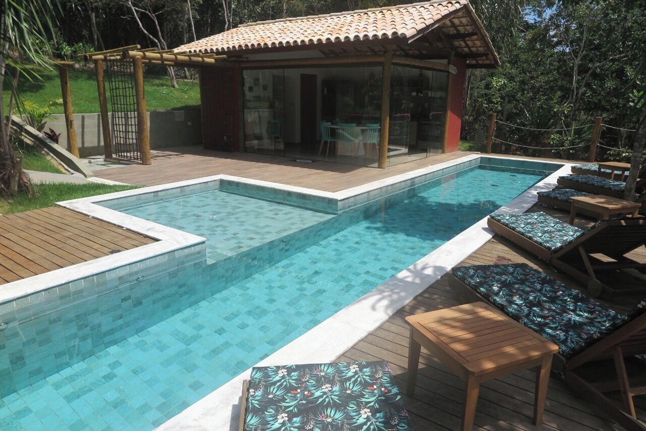 Ein Schwimmbecken mit Holzterrasse, Liegestühlen und einer überdachten Sitzgelegenheit.