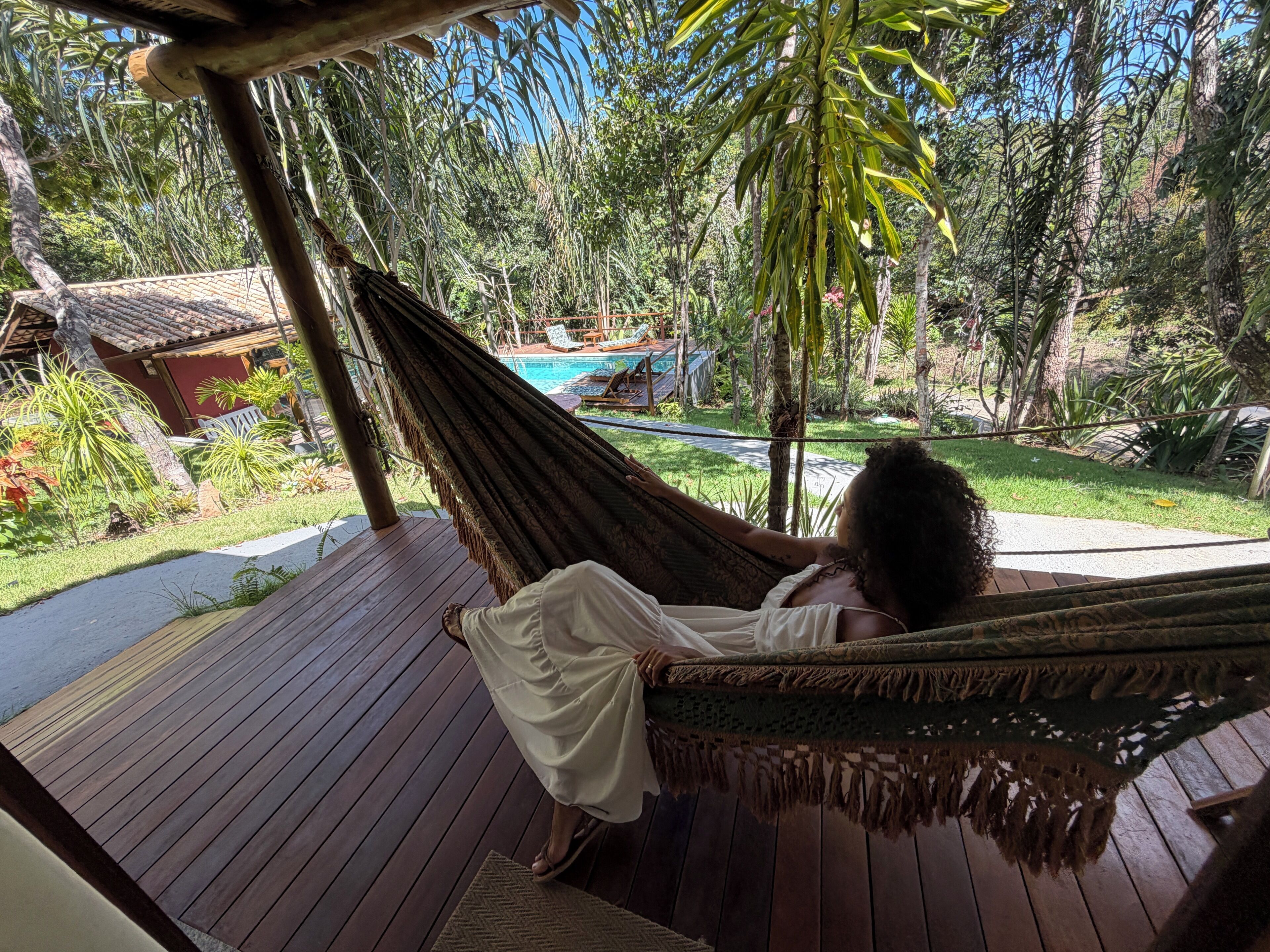 Eine Hängematte auf einer Holzterrasse mit Blick auf einen Pool und üppiges Grün.