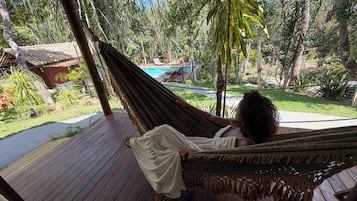 Eine Hängematte auf einer Holzterrasse mit Blick auf einen Pool und üppiges Grün.