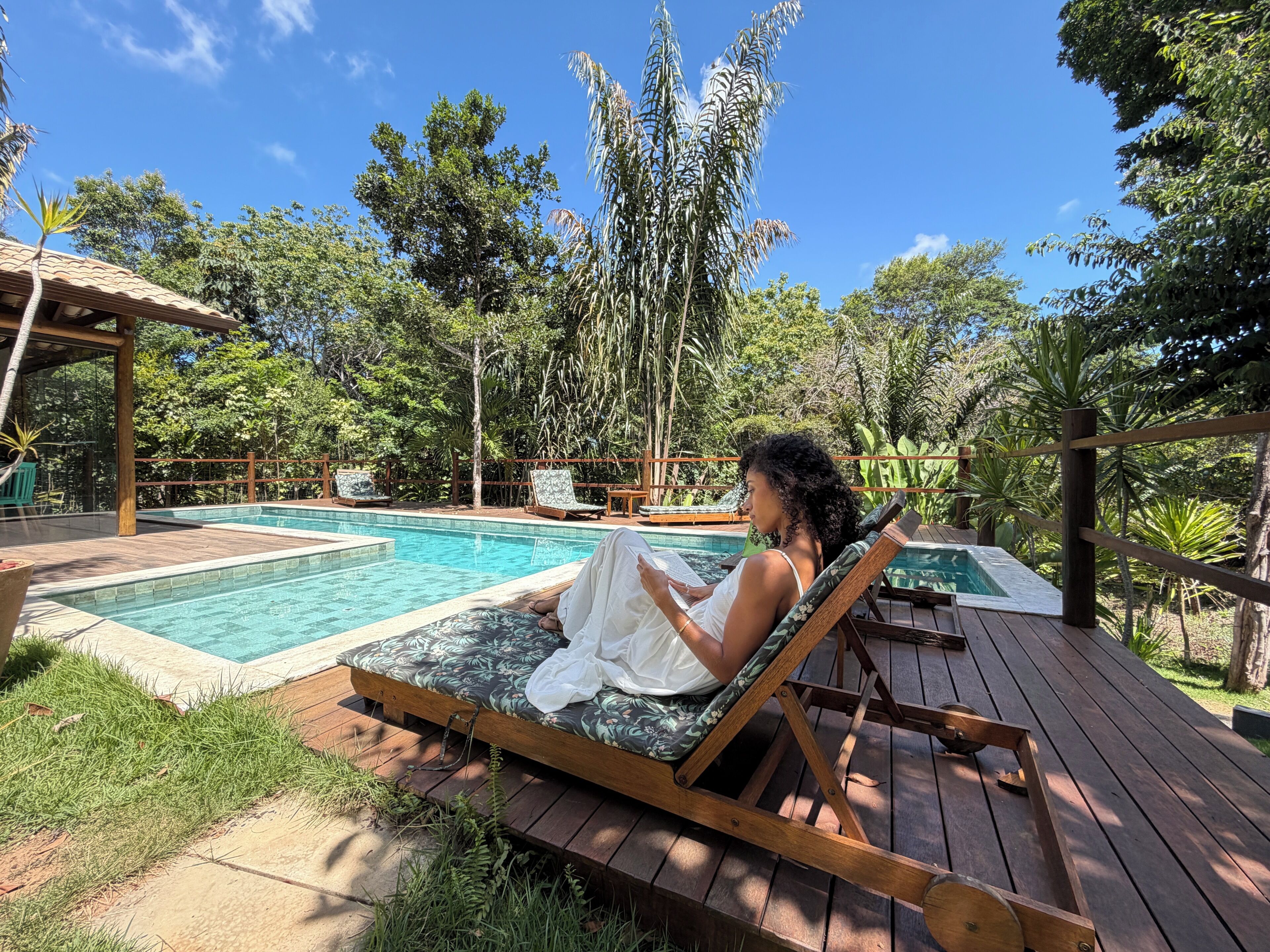 Ein Poolbereich mit Holzterrasse, Liegestühlen und einer Person, die ein Buch liest.