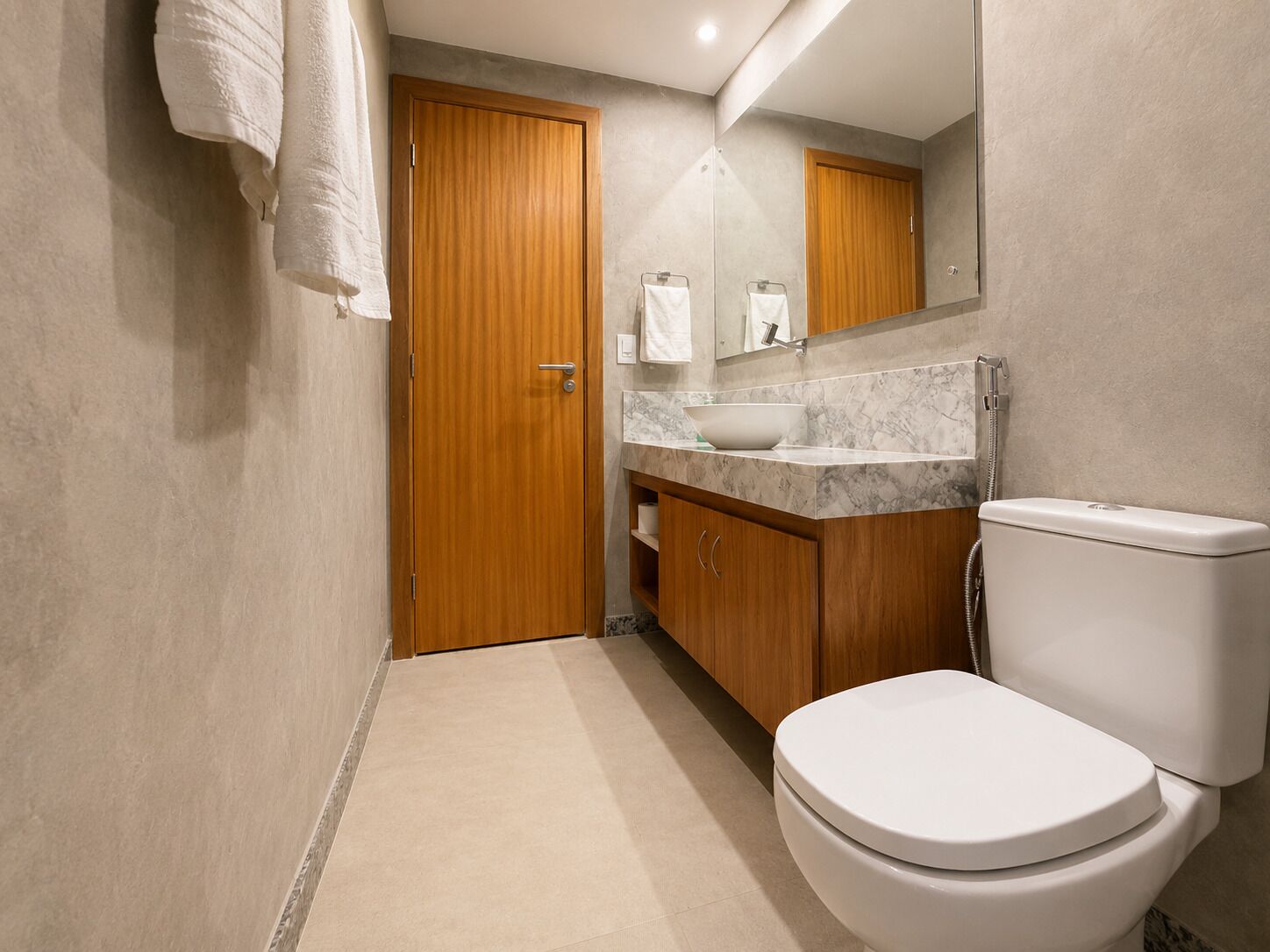 Un baño moderno con una puerta de madera, un inodoro blanco, un lavabo de mármol y un espejo sobre el lavabo.