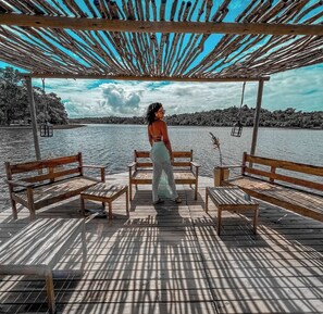 A wooden deck with benches and a pergola overlooking a body of water. - Refúgio By Bellatrix (Mata de São João)